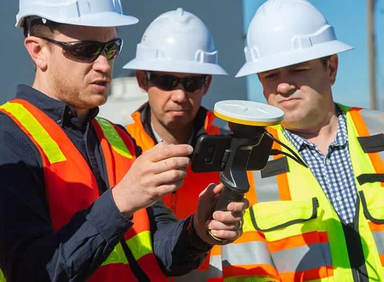 a group of men wearing safety vests and helmets looking at a cellphone